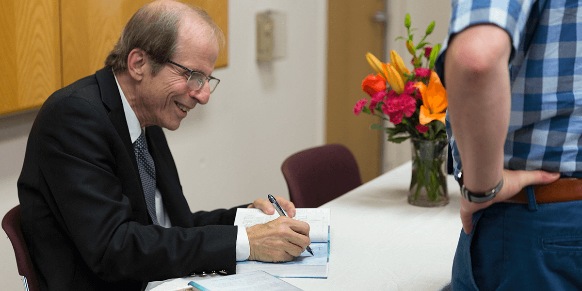 Michael Krasny signing a copy of his book while seated at a table